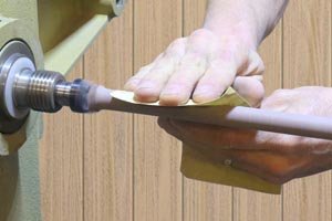 Sanding the handle on the wooden spoon with the lathe on.